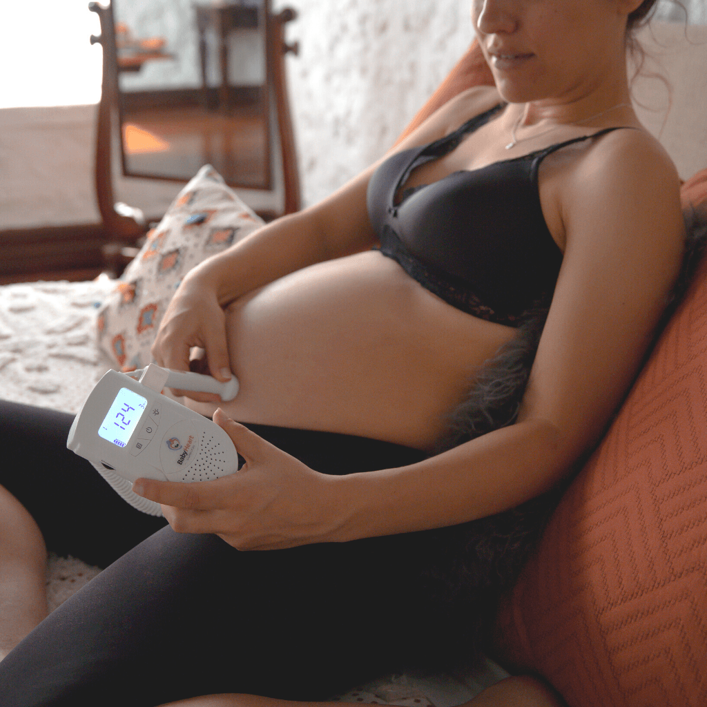 Pregnant worman sitting on her bed, using the Standard doppler listening to her baby's 124 heart rate displayed on the screen 