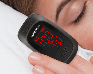 Woman laying down with eyes closed using the Jumper Fingertip Pulse Oximter. screen displays the pulse and Oxygen rate