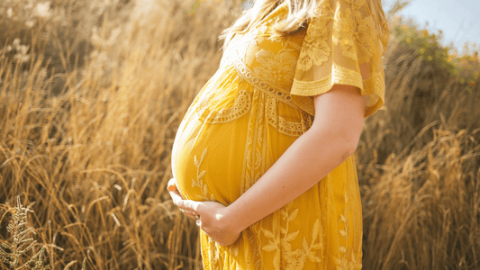 Happy pregnant woman holding belly in field in yellow dress