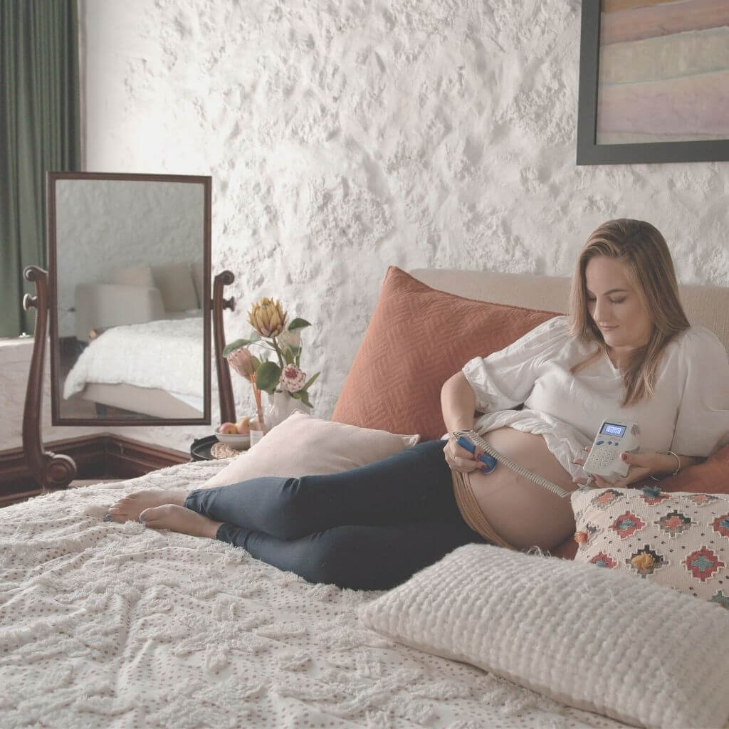 Pregnant woman laying comfortably on her bed using the BabyHeart Fetal Doppler listening to her babys heartbeat