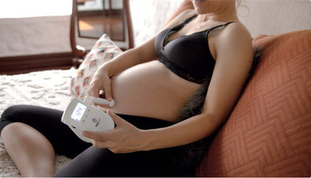 Pregnant woman sitting on her bed and using the BabyHeart Advanced fetal doppler on her belly