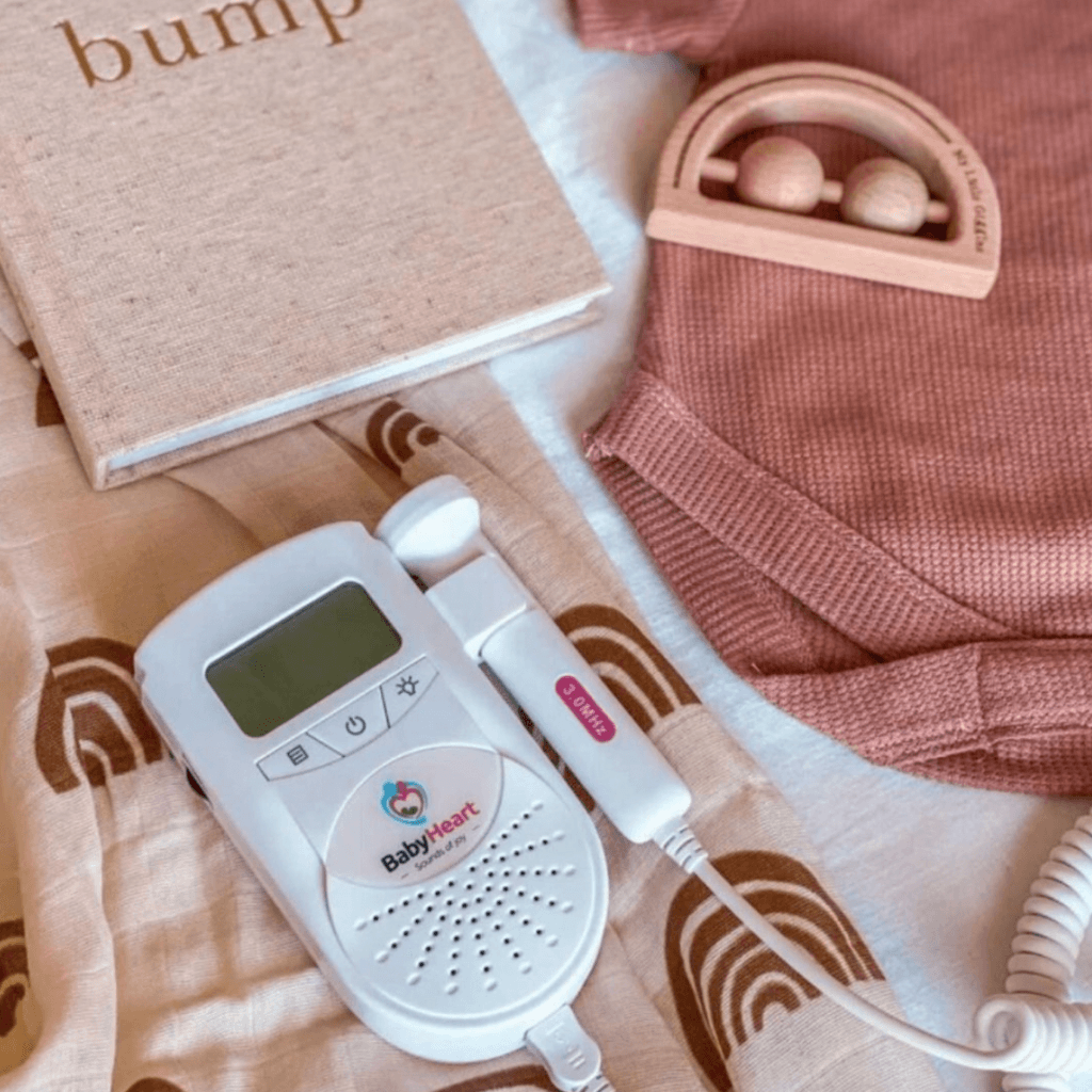 Product shot of the BabyHeart Fetal Doppler on a few baby clothes, notebook and a wooden toy