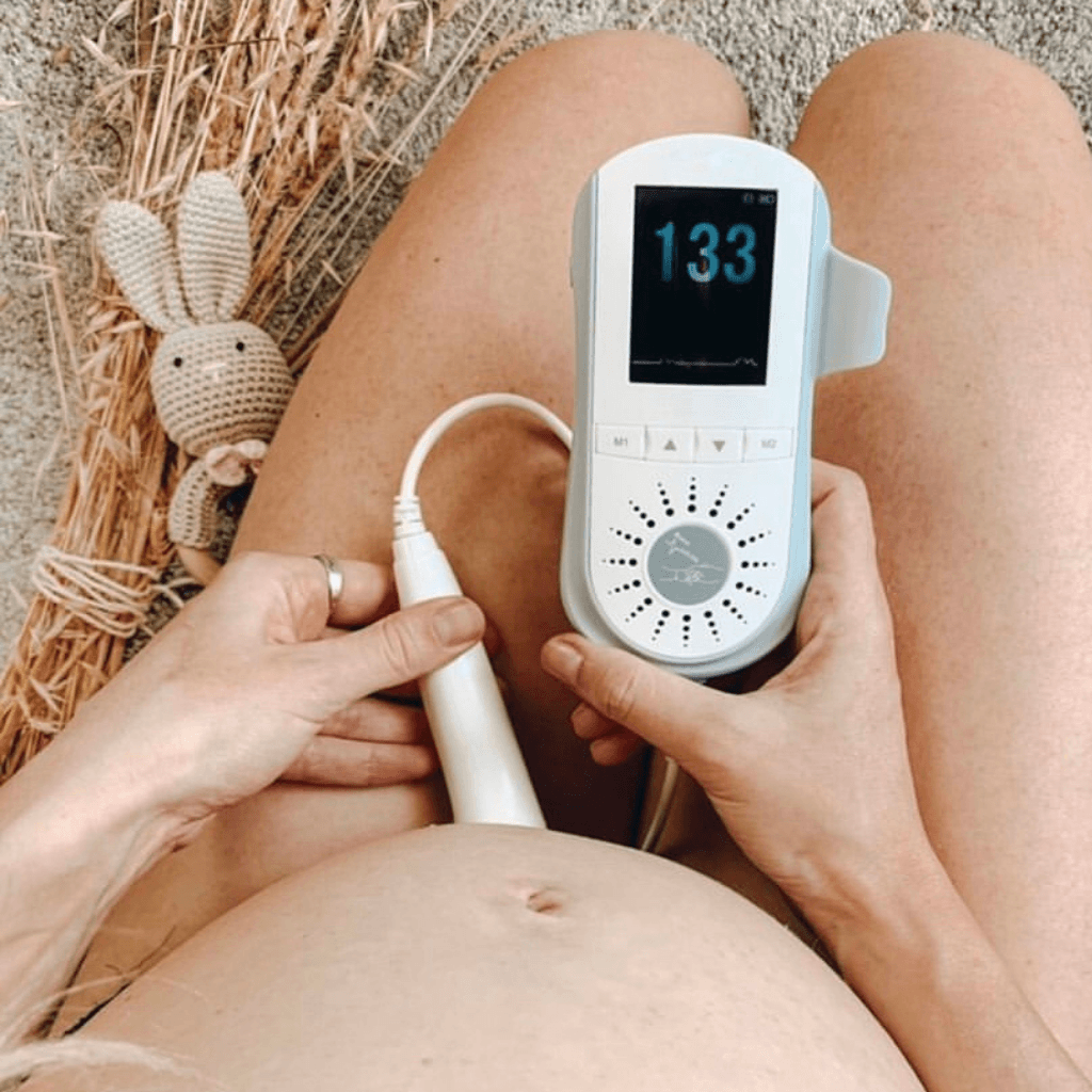 Pregnant woman kneeling on the carpet floor using the BabyHeart Premium doppler with the baby's heart rate 133 on the screen