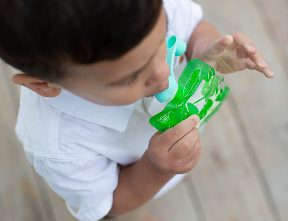 Lifestyle image of a toddler holding his green On the go Maxi pouch and enjoying his drink or meal.